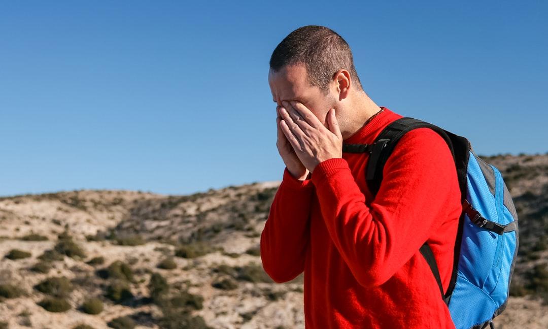 man wearing red crew-neck sweater with teal and black backpack outdoor during daytime Điều trị và Phòng ngừa Migraine (Đau nửa đầu) bằng Nurtec ODT